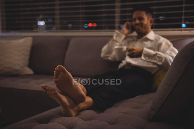 Homem falando no celular enquanto toma café em casa — Fotografia de Stock
