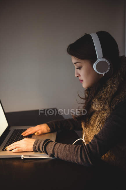 Женщина слушает наушники во время использования ноутбука в кабинете дома — стоковое фото