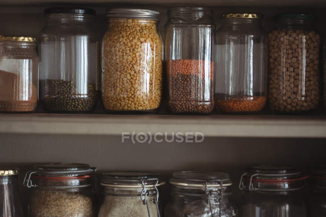 Крупный план различных бобов и чечевицы в банках на полке кухни — стоковое фото