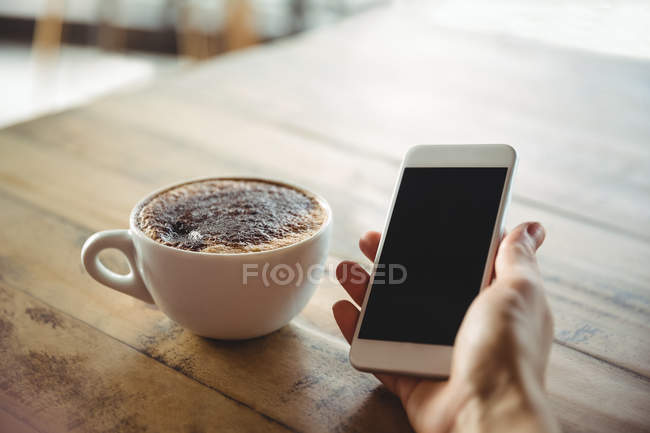Hand of a woman holding mobile phone in cafe — Stock Photo