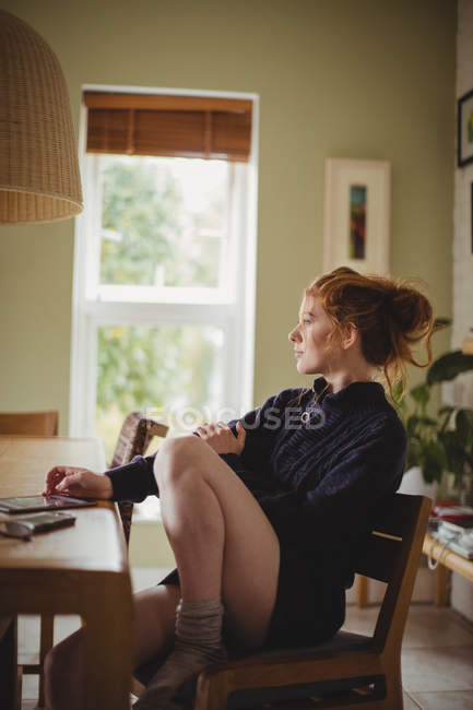 Femme réfléchie assise à table à la maison — Photo de stock
