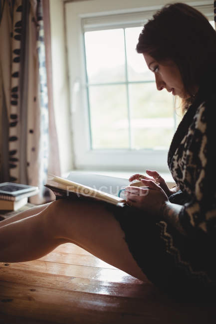 Жінка сидить біля вікна і читає книгу вдома — стокове фото