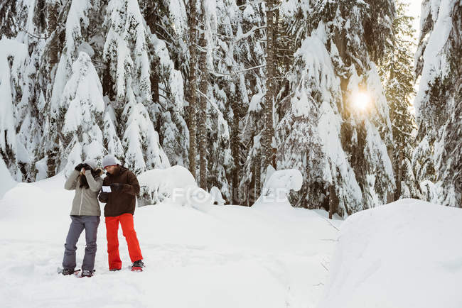 Casal com cartão de endereço olhando através de binóculos na paisagem nevada — Fotografia de Stock