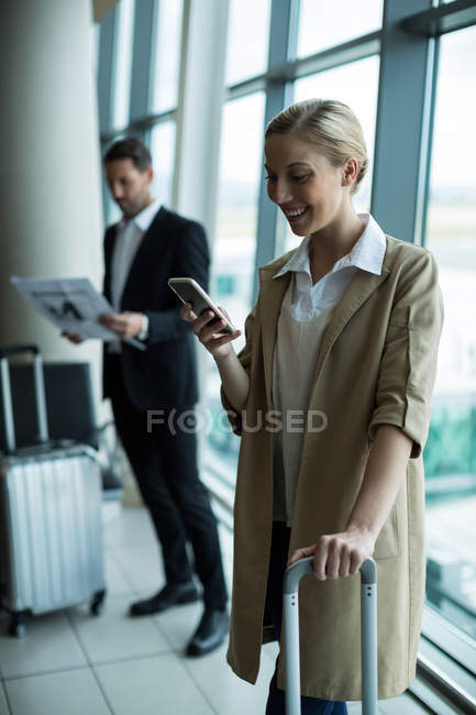 Бізнес-леді з багажем за допомогою мобільного телефону в аеропорту — стокове фото