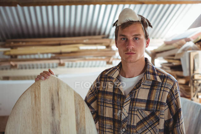 Front view of man standing with surfboard at workshop — Stock Photo