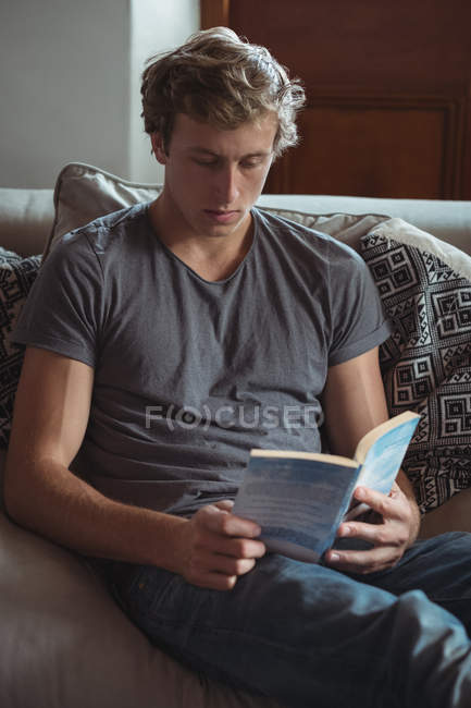Mann sitzt auf Sofa und liest Buch im Wohnzimmer — Stockfoto