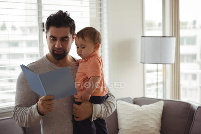 Отец читает книгу, держа ребенка дома. — стоковое фото