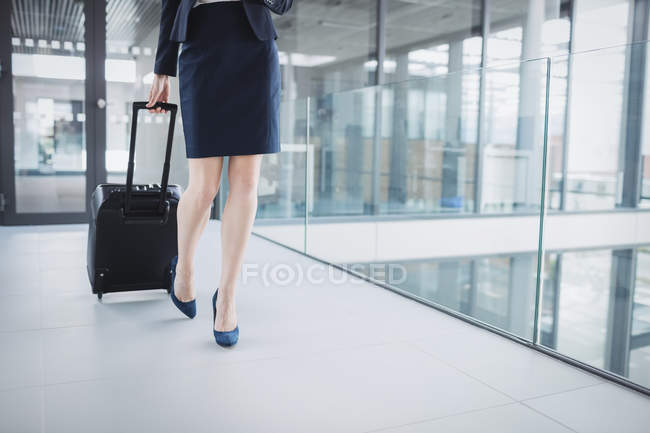 Низкий сегмент деловой женщины с чемоданом, идущей по офисному коридору — стоковое фото
