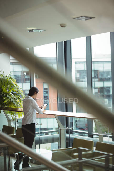 Businesswoman leaning on railing and using mobile phone at office — Stock Photo
