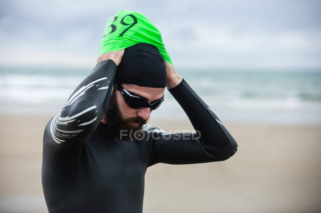 Спортсмен в мокром костюме в плавательной шапке на пляже — стоковое фото