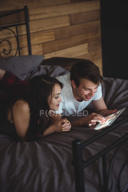 Casal deitado na cama usando tablet digital no quarto em casa — Fotografia de Stock