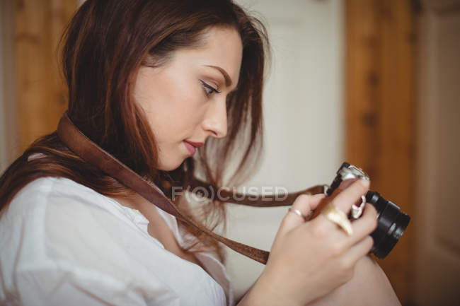 Belle femme regardant des photos sur l'appareil photo numérique à la maison — Photo de stock