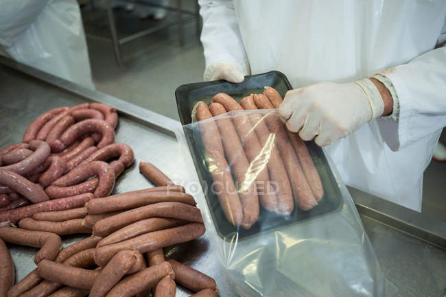 Seção média de açougueiro embalando salsichas cruas na fábrica de carne — Fotografia de Stock