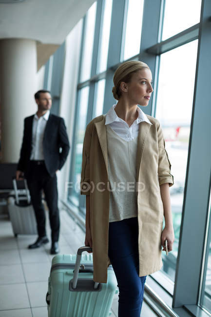 Geschäftsfrau mit Gepäck blickt durch Glasfenster am Flughafen — Stockfoto
