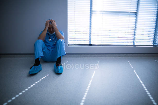 Depressed surgeon leaning against wall at hospital — Stock Photo