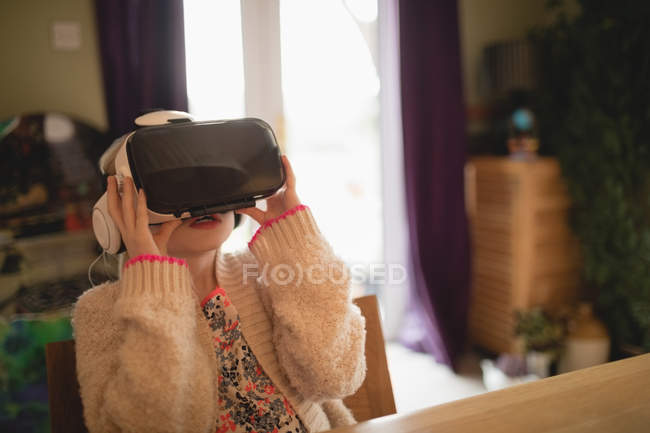 Дівчина сидить за столом і використовує віртуальну гарнітуру вдома — стокове фото