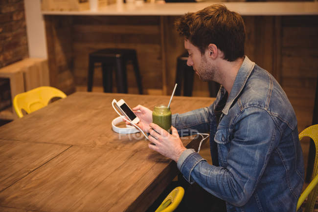 Чоловік використовує мобільний телефон, маючи сік в кафе — стокове фото