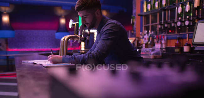 Cantinero manteniendo registros en el mostrador en el bar - foto de stock