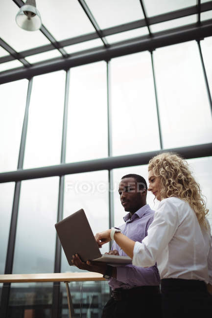 Керівники бізнесу обговорюють ноутбук в офісному коридорі — стокове фото