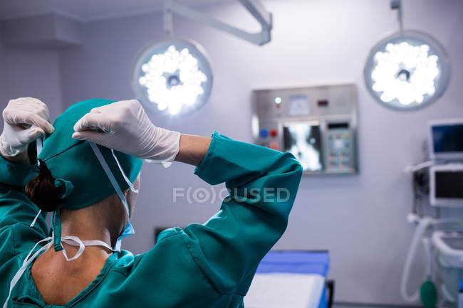 Rear view of female surgeon wearing surgical mask in operation theater of hospital — Stock Photo