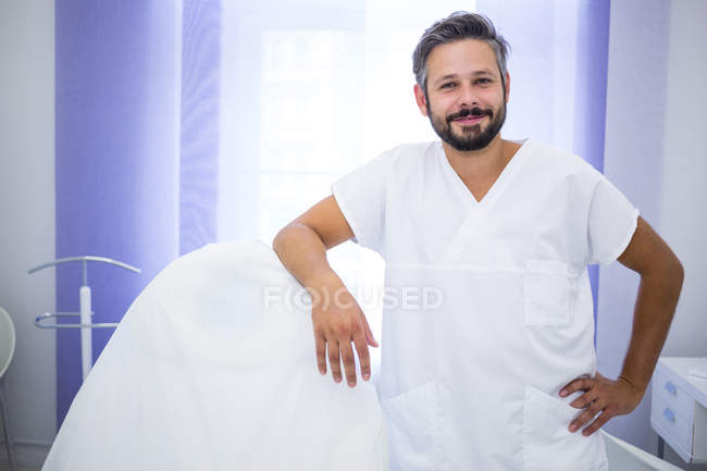 Портрет улыбающегося врача, стоящего в клинике и опирающегося на стул — стоковое фото