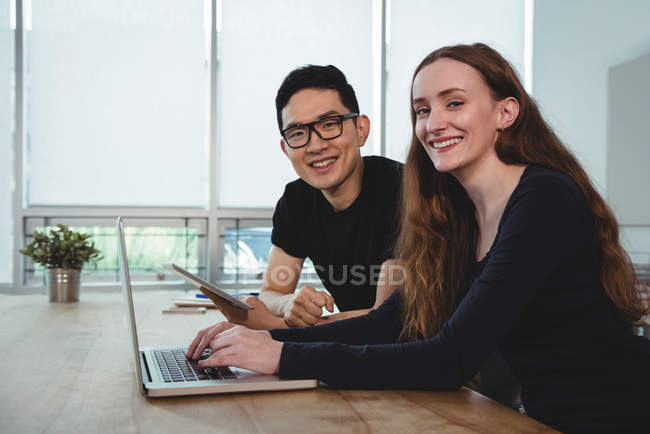 Retrato de executivos de negócios sorridentes com tablet digital e laptop sentado no escritório — Fotografia de Stock