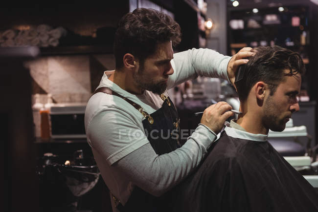 Homem recebendo cabelo aparado por cabeleireiro com navalha na barbearia — Fotografia de Stock