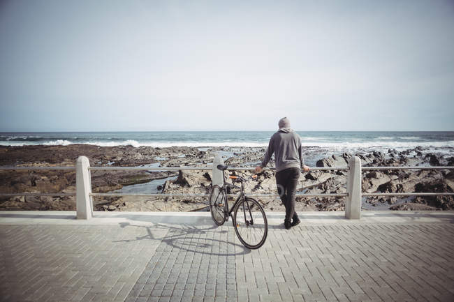Вид ззаду на невпізнаваного чоловіка, що стоїть з велосипедом біля моря — стокове фото