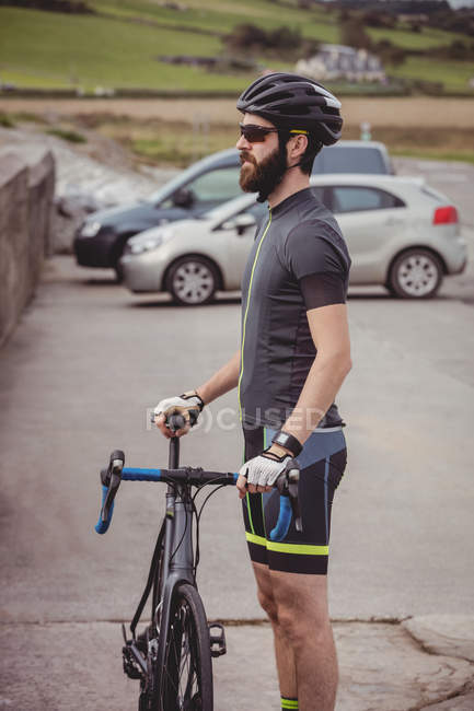 Спортсмен, стоящий с велосипедом на дороге с автомобилями — стоковое фото
