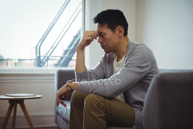 Напряженный человек сидит на диване в гостиной на дому — стоковое фото