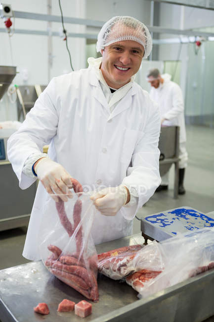 Retrato del carnicero macho empacando salchichas crudas en fábrica de carne - foto de stock