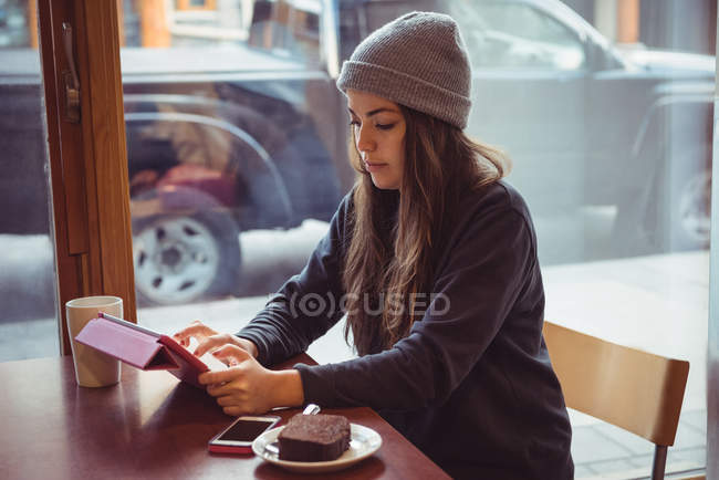 Woman in winter clothing using digital tablet in restaurant — Stock Photo