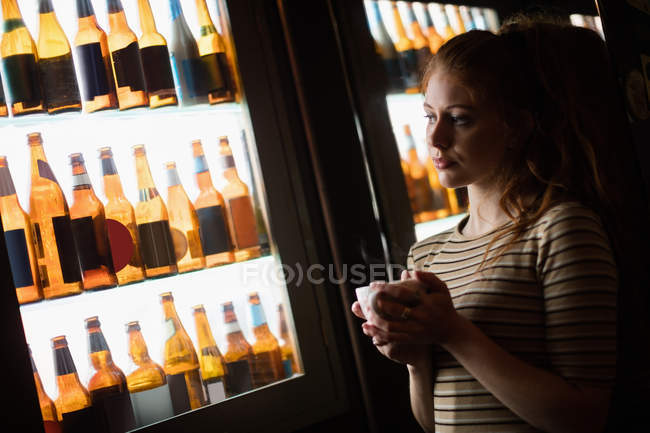Femme réfléchie tenant tasse de café dans le bar — Photo de stock