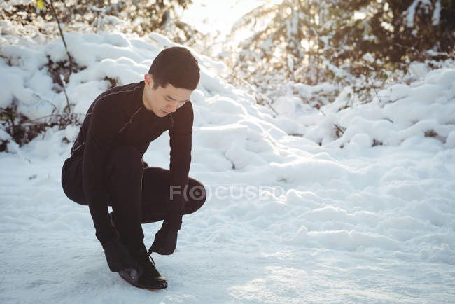 Чоловік зав'язує шнурки в лісі взимку — стокове фото