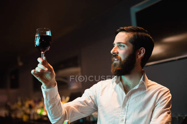 Barman regardant un verre de vin rouge au comptoir du bar — Photo de stock