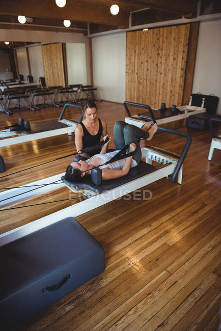 Instructor helping a woman while practicing pilates in fitness studio — Stock Photo
