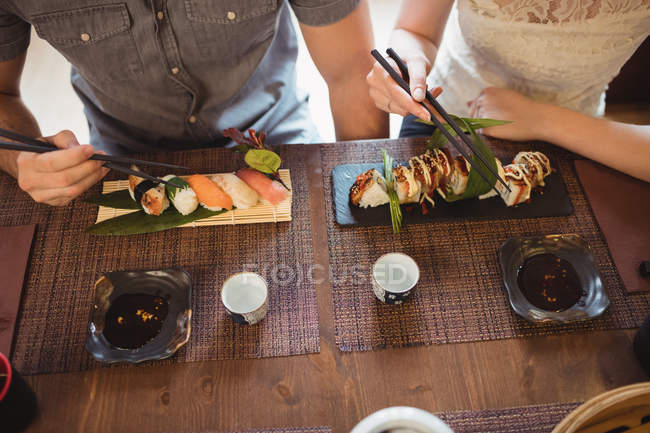 Sección media de la pareja tomando sushi en el restaurante - foto de stock