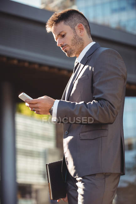 Homme d'affaires utilisant un téléphone portable près d'un immeuble de bureaux — Photo de stock