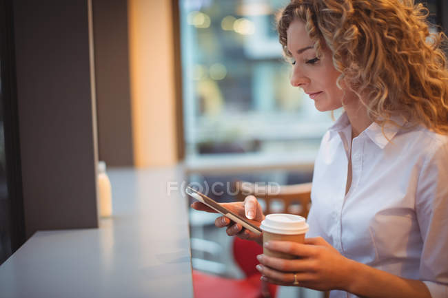 Mulher loira usando telefone celular no balcão na cafetaria — Fotografia de Stock
