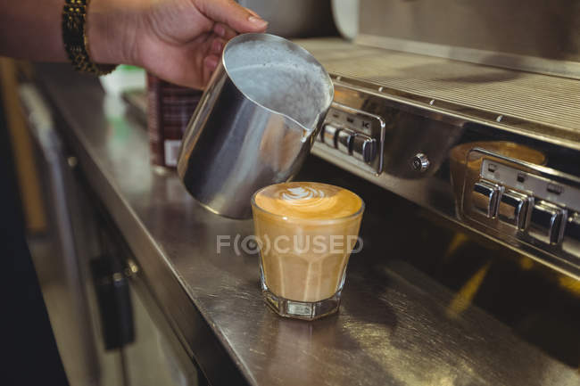 Waitress pouring milk into coffee cup at counter in cafe — Stock Photo
