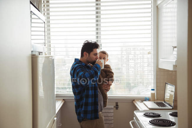 Vater trinkt Kaffee, während er Baby in Küche hält — Stockfoto