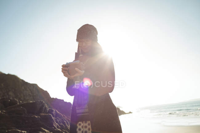 Donna sorridente guardando le foto sulla macchina fotografica digitale in spiaggia — Foto stock