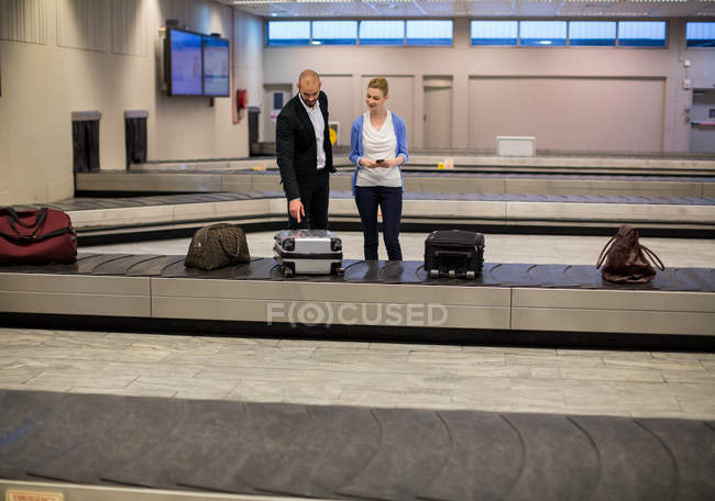 Casal esperando por bagagem na área de reclamação de bagagem no terminal do aeroporto — Fotografia de Stock