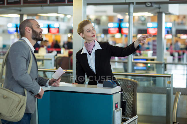 Airline check-in attendant showing direction to commuter at check-in counter in airport terminal — Stock Photo