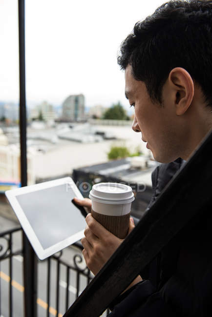 A meio da seção do homem usando tablet digital enquanto toma café na varanda — Fotografia de Stock