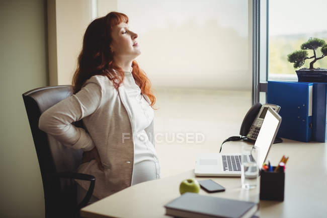 Беременная деловая женщина сдерживает себя, сидя на кресле в офисе — стоковое фото