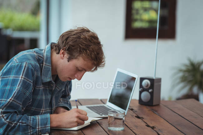 Hombre sentado en la mesa y escribiendo notas en casa - foto de stock