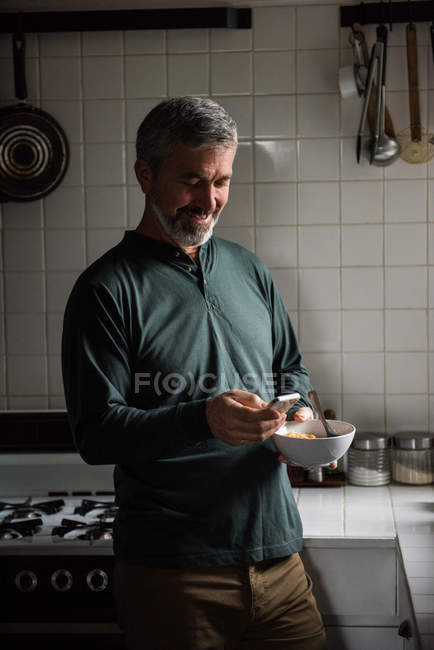 Homem usando telefone celular enquanto toma café da manhã na cozinha em casa — Fotografia de Stock