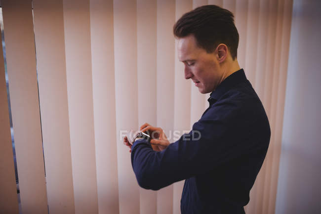Masculino executivo verificando horário no smartwatch no escritório — Fotografia de Stock
