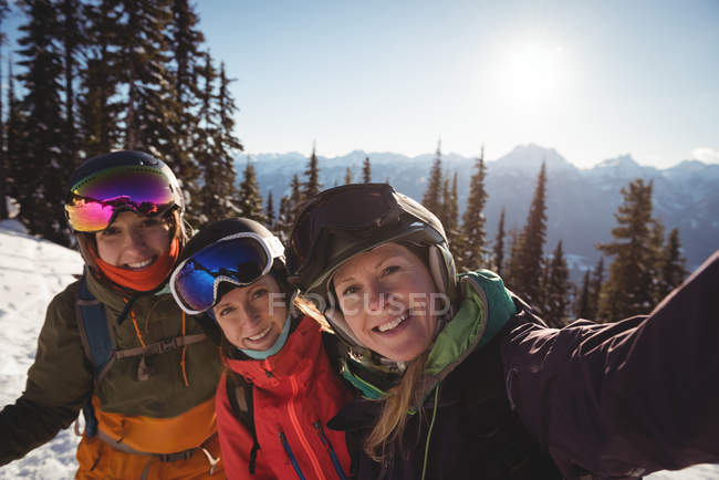 Retrato de tres esquiadoras de pie juntas en montañas cubiertas de nieve - foto de stock